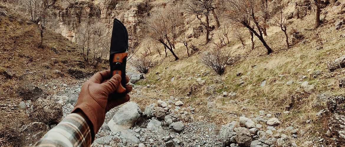 Hand with leather glove holding hunting knife in sheath while hiking